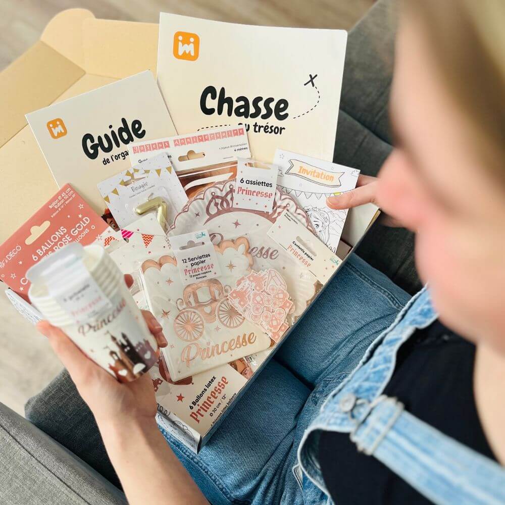 Personne ouvrant la box anniversaire Jimily sur le thème Princesse, découvrant le contenu : décorations, vaisselle jetable, bougie, chasse au trésor, guide pour les parents.