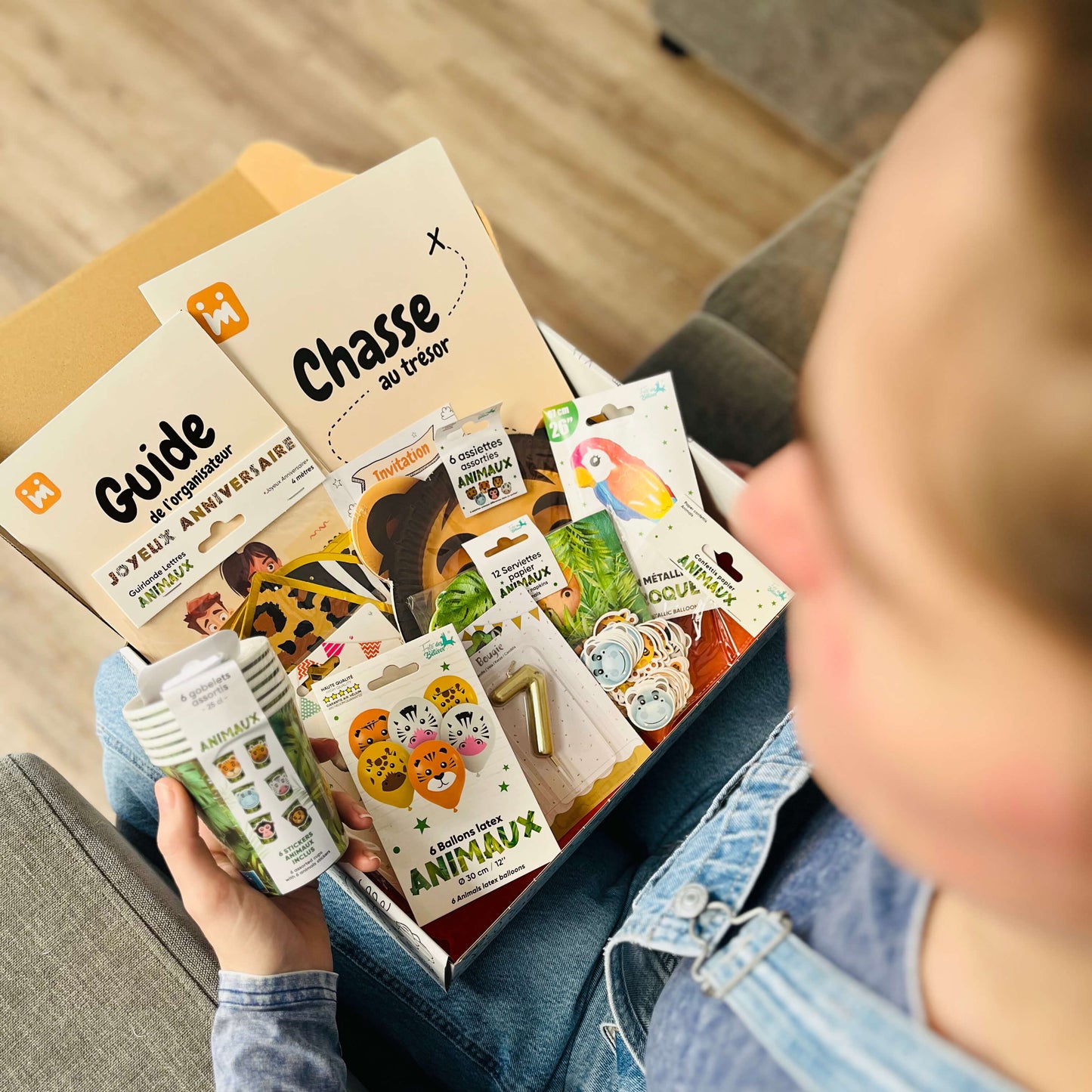 Personne ouvrant la box anniversaire Jimily sur le thème Safari, découvrant le contenu : décorations, vaisselle jetable, bougie, chasse au trésor, guide pour les parents/
