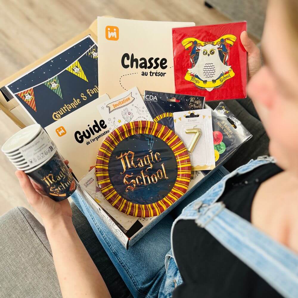 Personne ouvrant la box anniversaire Jimily sur le thème de la Magie, découvrant le contenu :  décorations, bougie, vaisselle jetable, chasse au trésor, guide pour les parents.