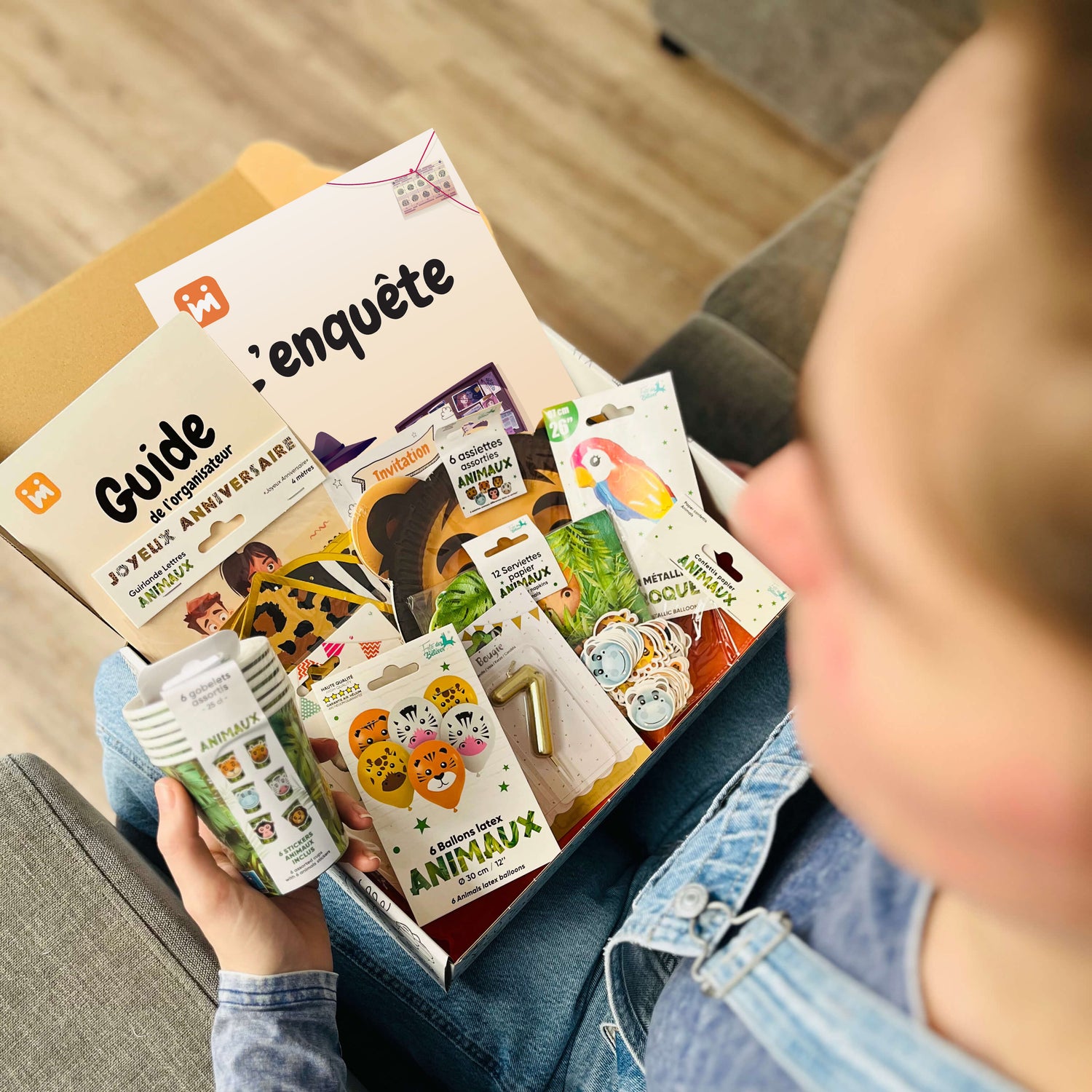 Personne ouvrant la box anniversaire Jimily sur le thème Safari, découvrant le contenu : décorations, vaisselle jetable, bougie, enquête, guide pour les parents